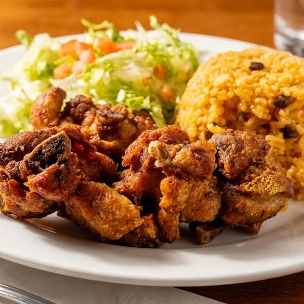 Fried pork chunks with yellow rice and a side salad on a white plate.