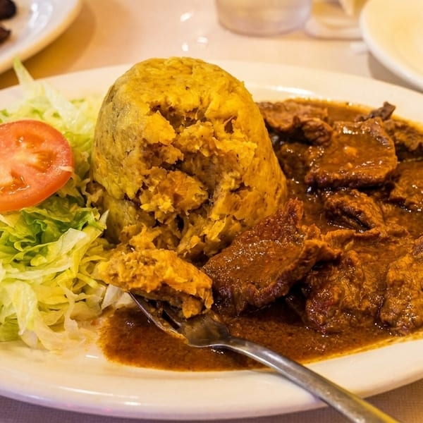 Mofongo with stewed beef, shredded lettuce, and a tomato slice on a white plate.