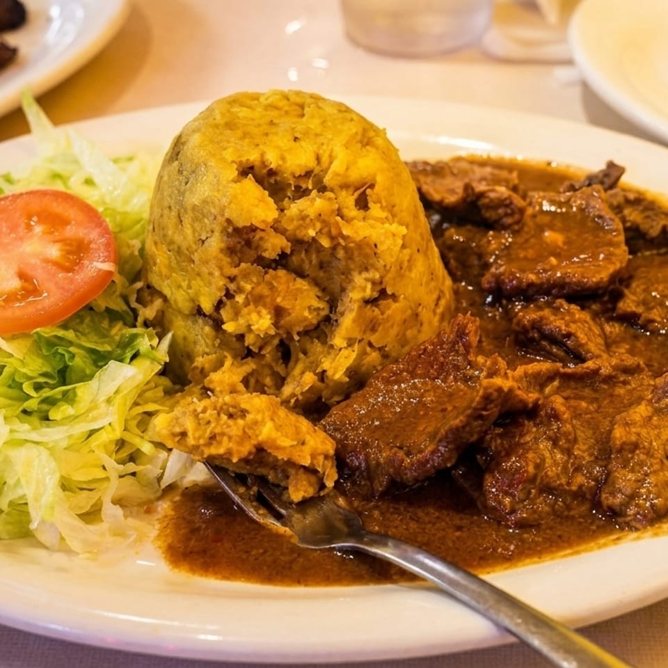 Mofongo with stewed beef, shredded lettuce, and a tomato slice on a white plate.